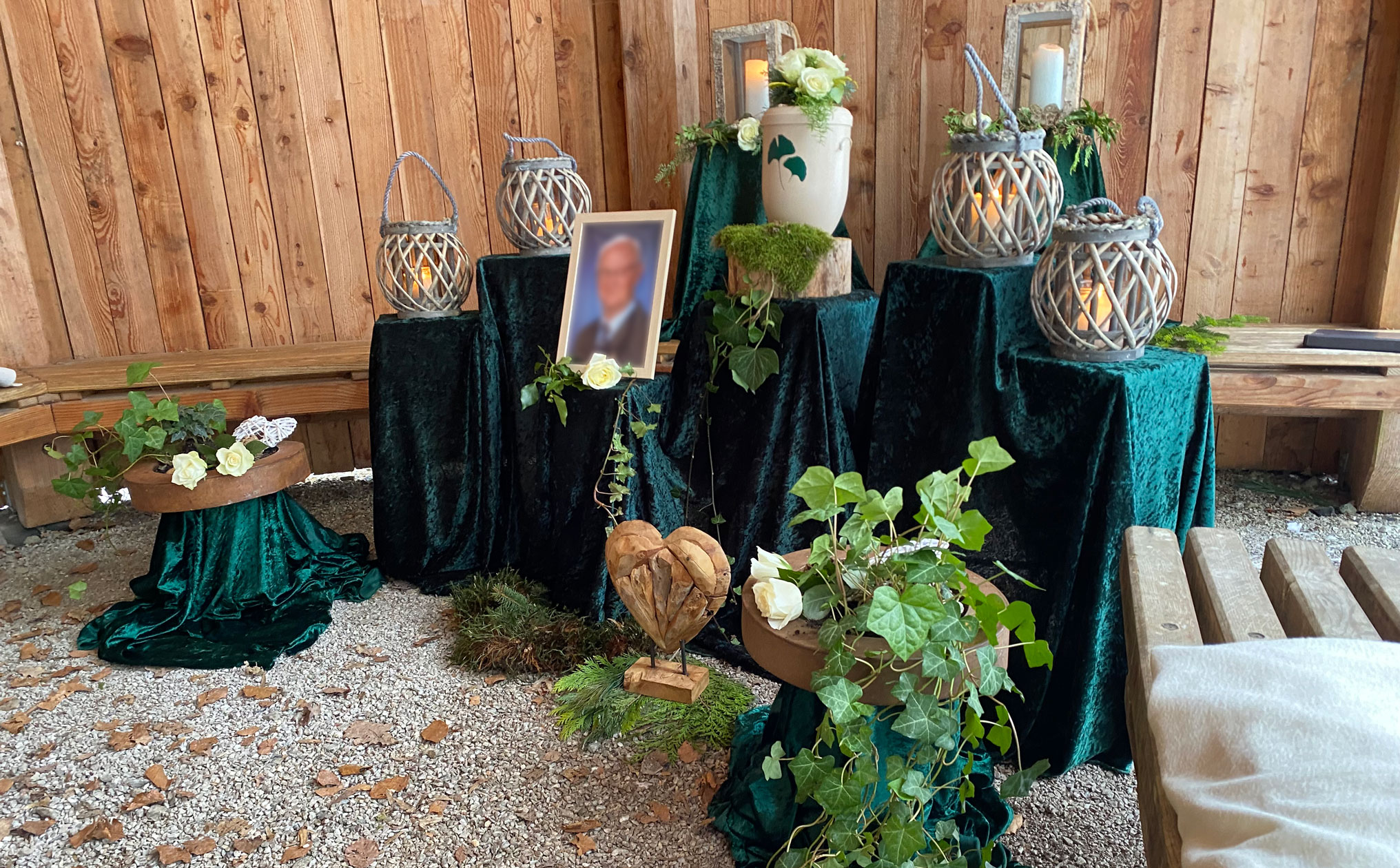 Naturnahe Abschiednahme mit einer Urne, Holzlaternen mit Kerzen und grüner Dekoration in einer rustikalen Umgebung mit Holzwänden.